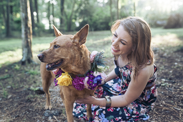 smiling dog in floral wreath, woman in sleeveless floral dress, celebrating human-dog bond