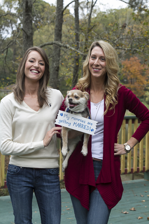 engagement photos of dog and 2 women, dog wearing "save the date sign"
