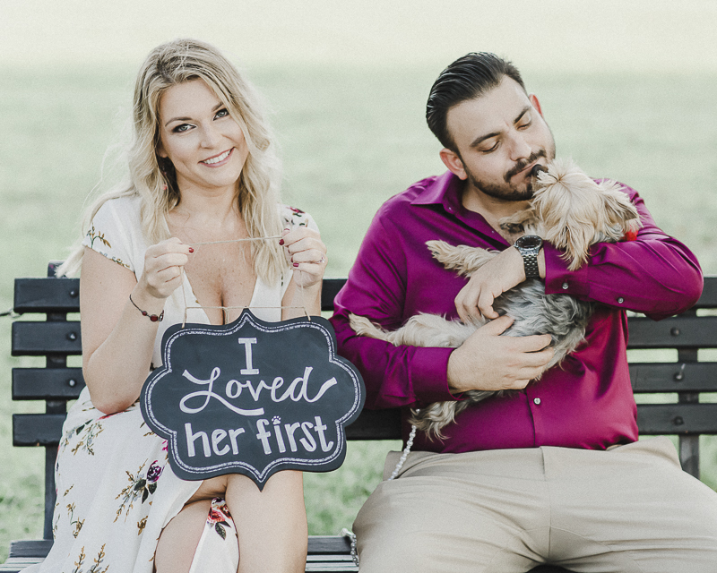 woman holding "I Loved Her First" sign while man cuddles dog, fun pet friendly engagement ideas, ©M Harris Studios | DC Engagement photos with Yorkie