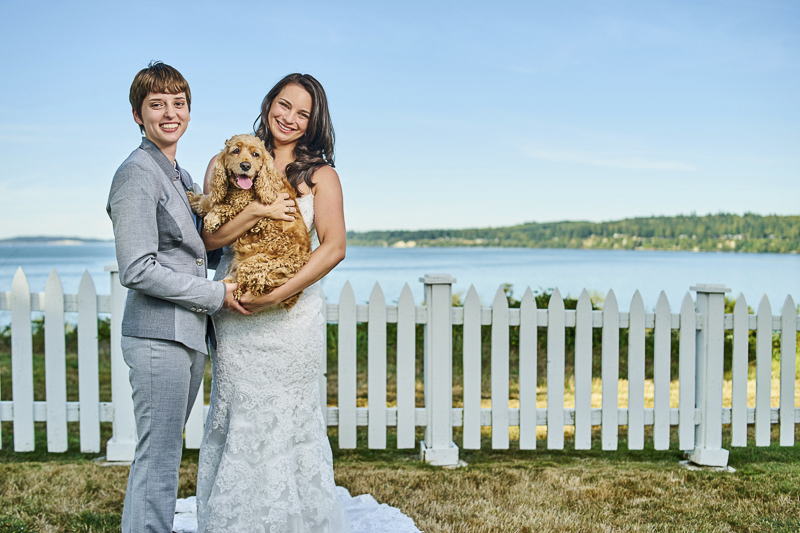dog friendly LGBTQ wedding couple holding their dog in front of white picket fence, ©Lavender Bouquet Photography